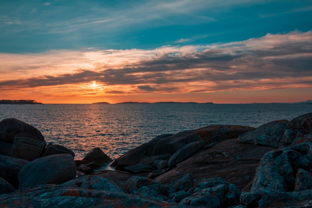 rocky shore under cloudy sky during sunset