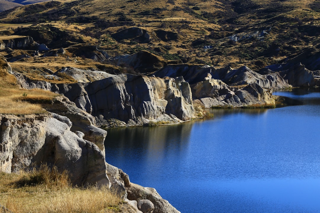 brown rocky mountain beside blue lake during daytime