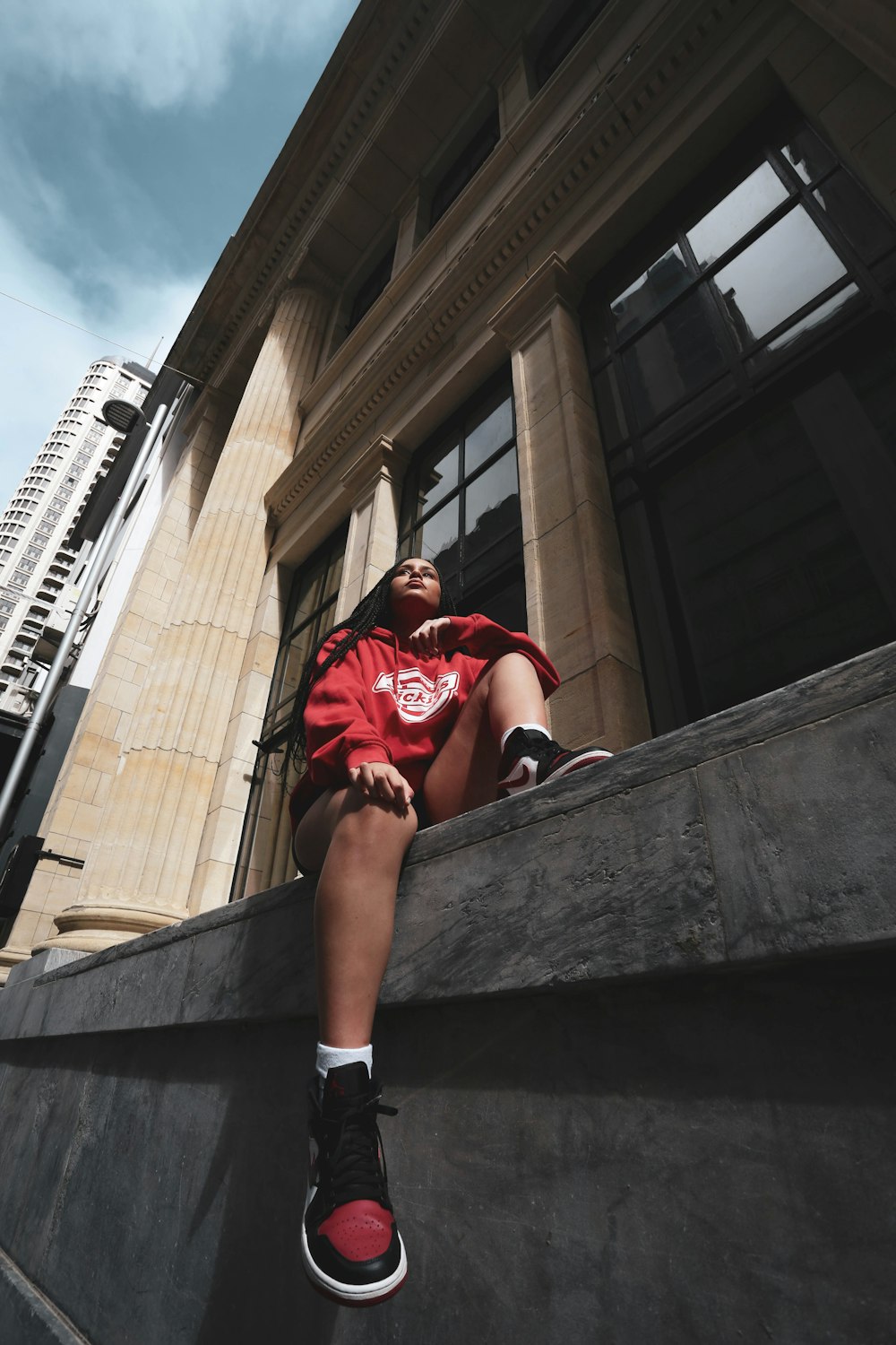 woman in red shirt sitting on concrete wall during daytime