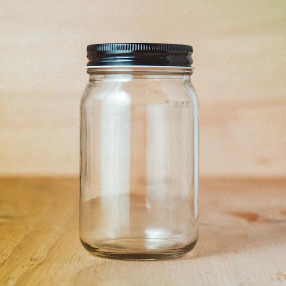 An empty glass jar with a black metal lid on a wooden surface