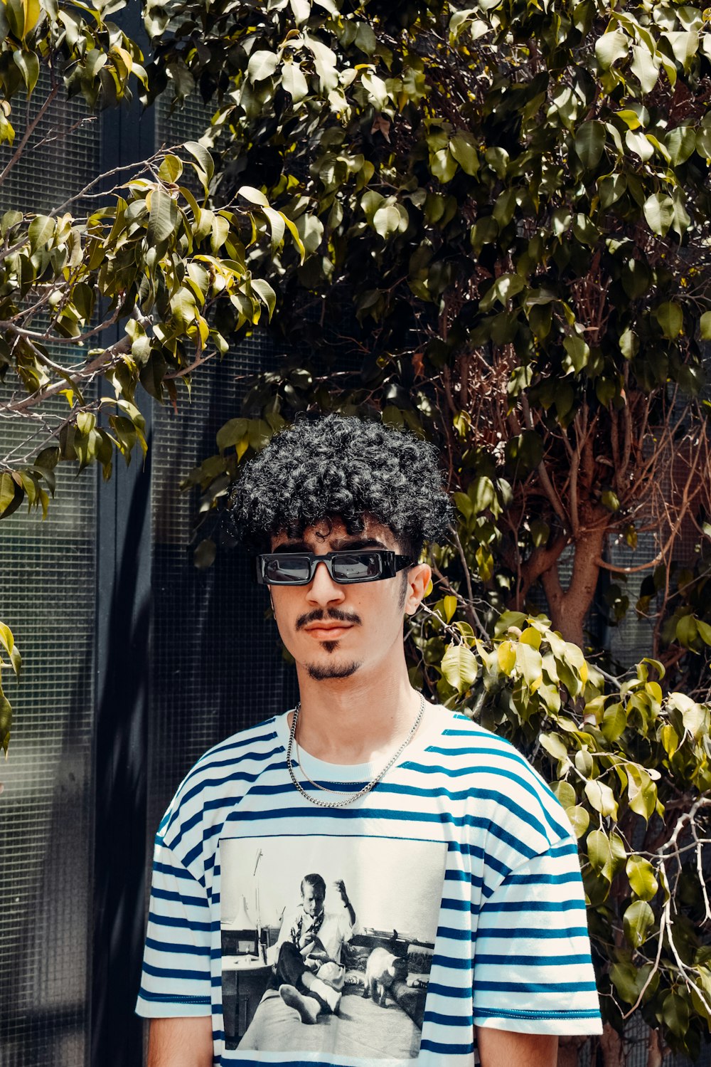 man in blue and white striped crew neck shirt wearing black sunglasses standing beside green plants
