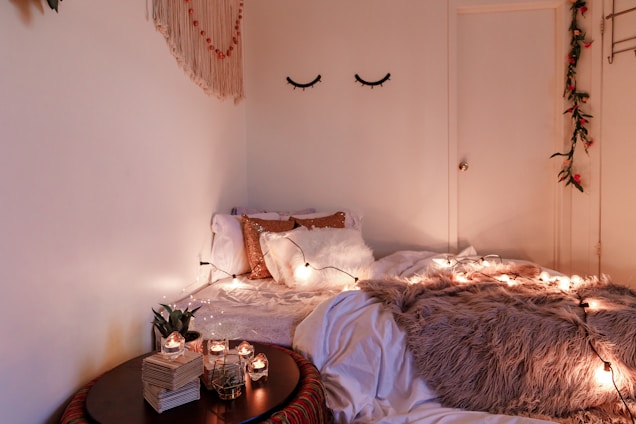 A softly lit bedroom corner styled with pastel cushions, delicate fairy lights, and a small DIY vase on a white desk.