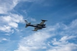 A small airplane flies through a blue sky with scattered white clouds. The tail number N21FC is visible on the aircraft.