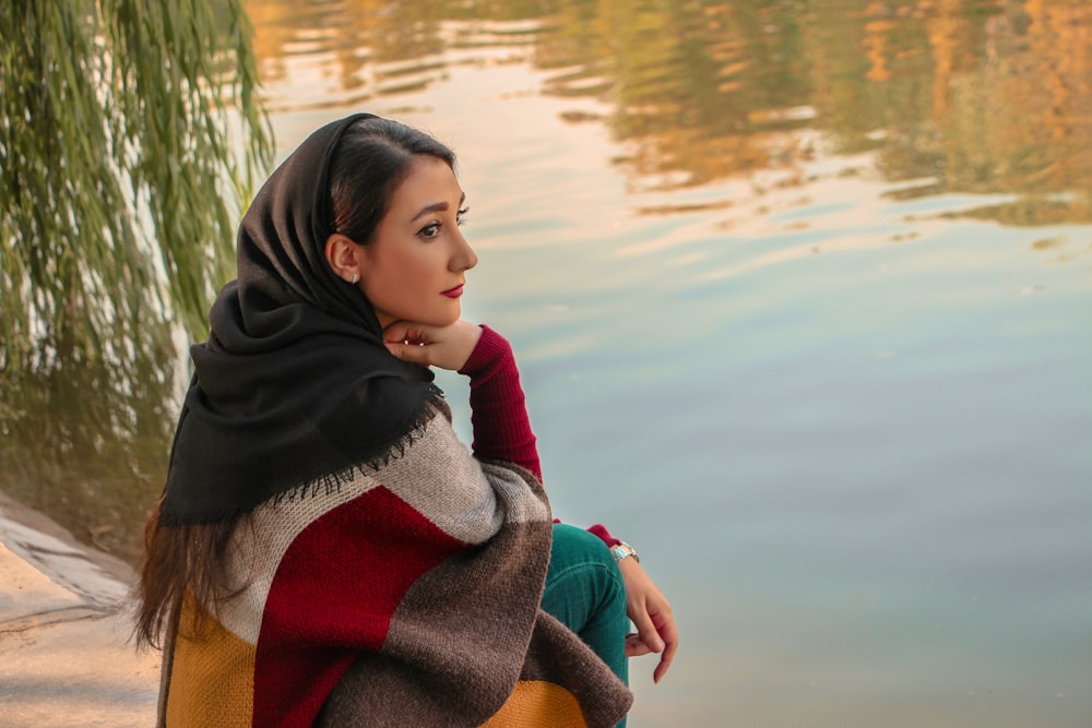 woman in red and white sweater sitting on brown wooden dock during daytime