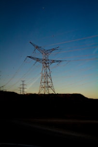 gray electric towers on brown hill under blue sky during daytime