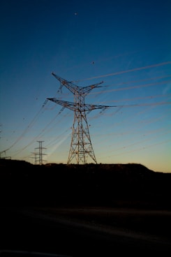 gray electric towers on brown hill under blue sky during daytime