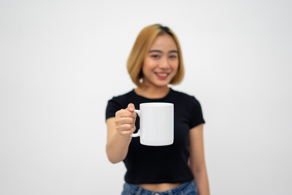 Femme en T-shirt à col rond noir tenant une tasse en céramique blanche