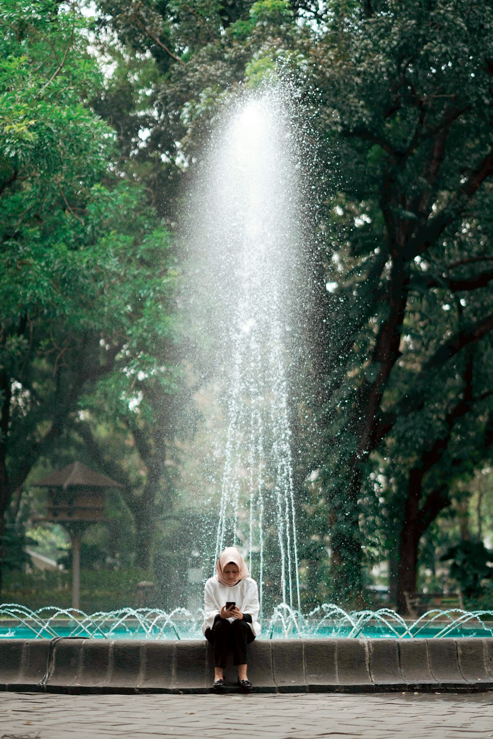 Mujer en camisa blanca de manga larga de pie cerca de la fuente de agua durante el día