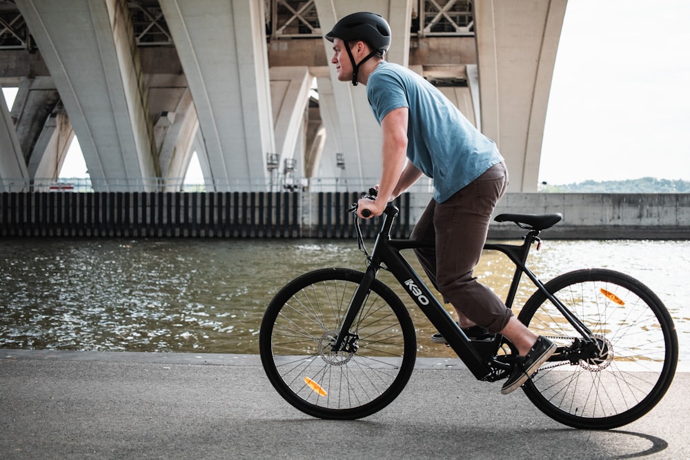 homme en t-shirt blanc conduisant un vélo noir sur une route en béton gris pendant la journée