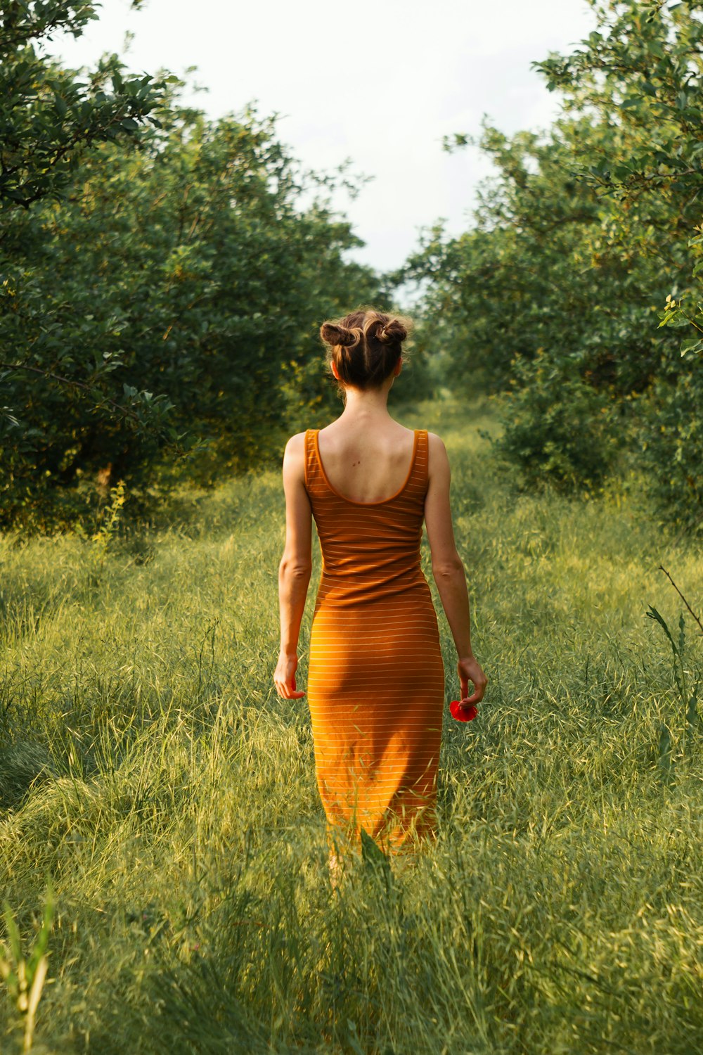 낮 동안 푸른 잔디밭에 서 있는 주황색 탱크 드레스를 입은 여자
