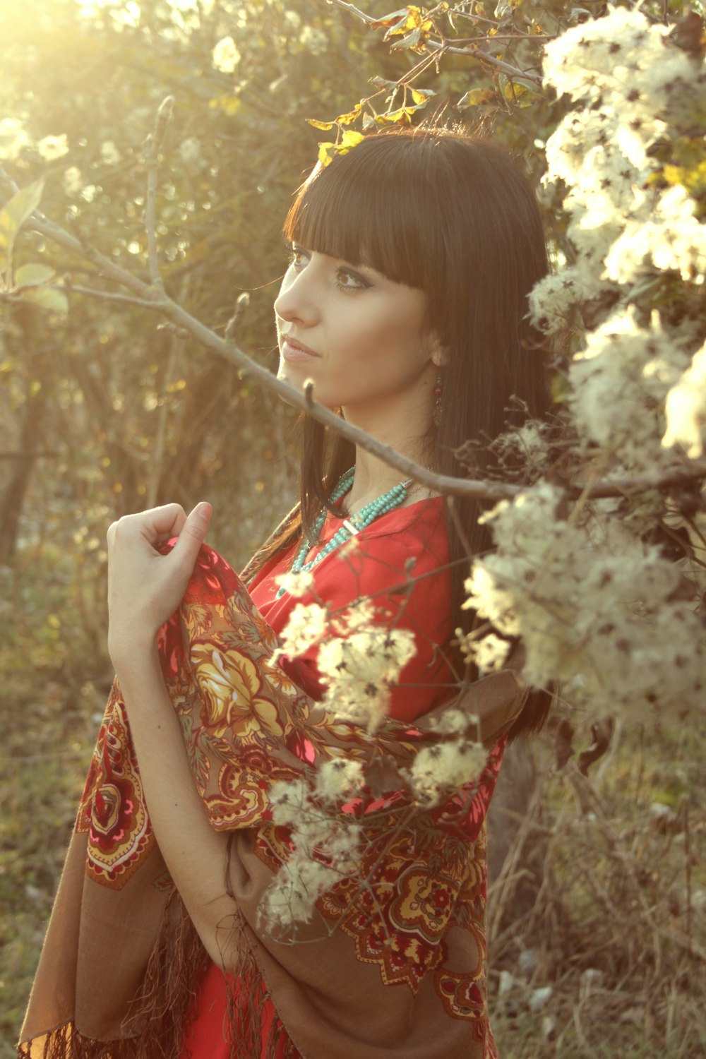 woman in red and white floral dress standing near brown leaf tree during daytime