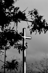 grayscale photo of cross under cloudy sky