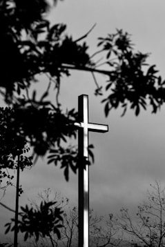 grayscale photo of cross under cloudy sky