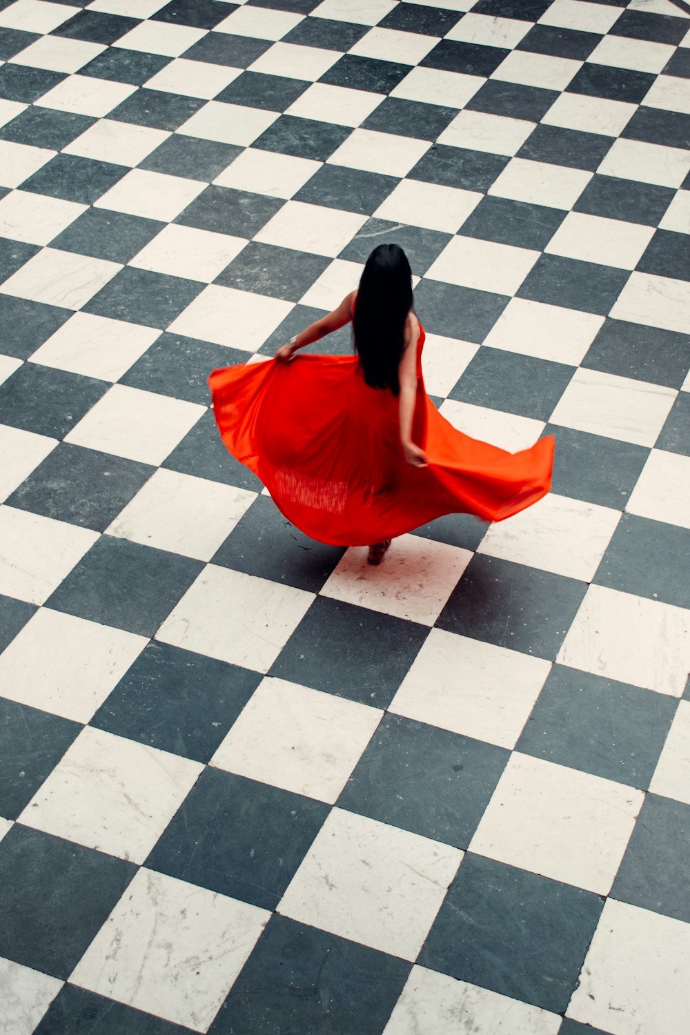 femme en robe rouge marchant sur des carreaux de sol gris et blancs