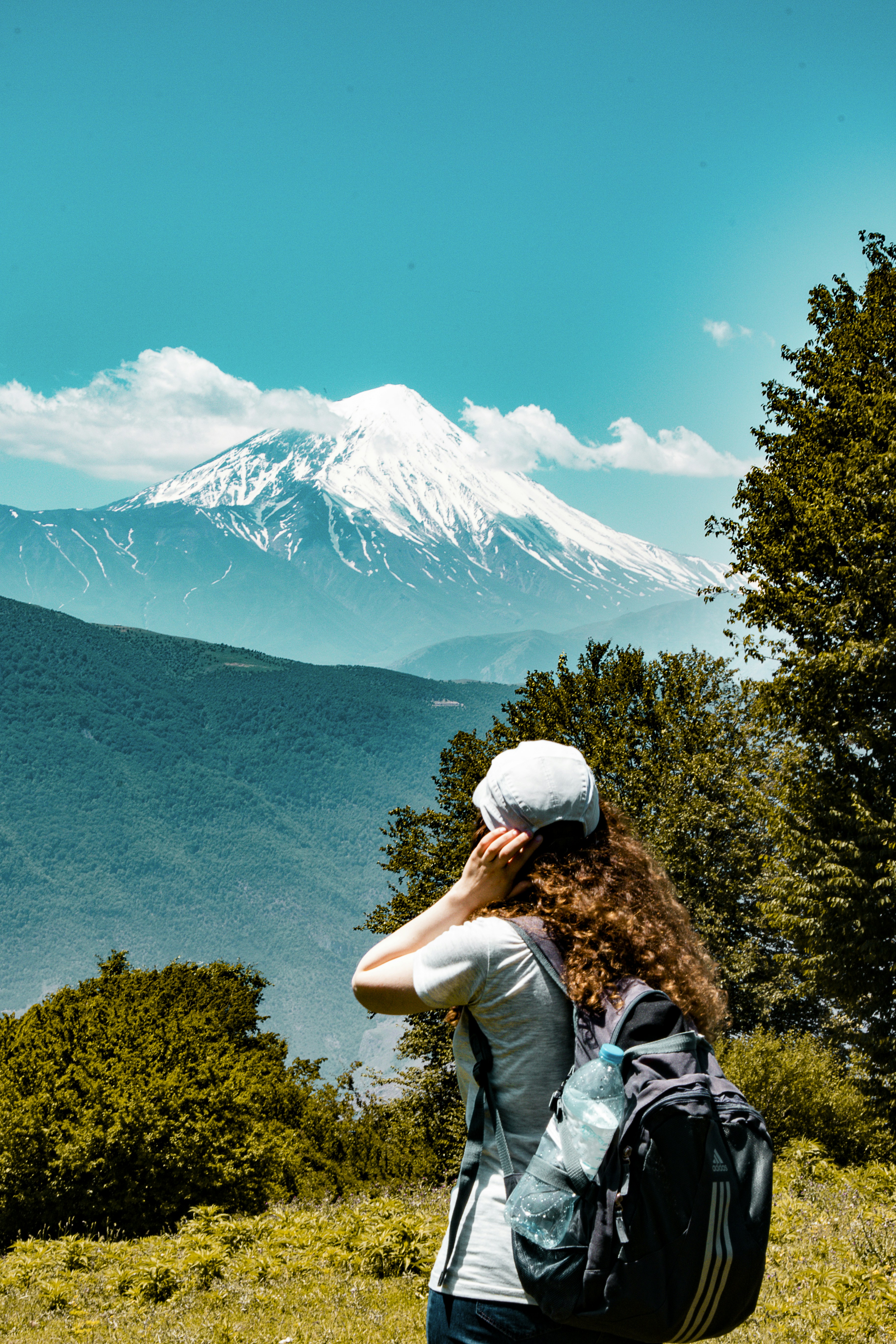 緑のシャツと灰色の帽子をかぶった男性が緑の草原に立って雪を見ている