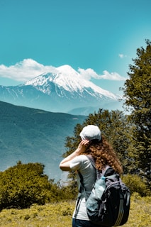 man in green shirt and gray cap standing on green grass field looking at snow covered