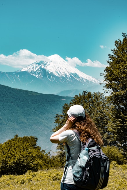 man in green shirt and gray cap standing on green grass field looking at snow covered
