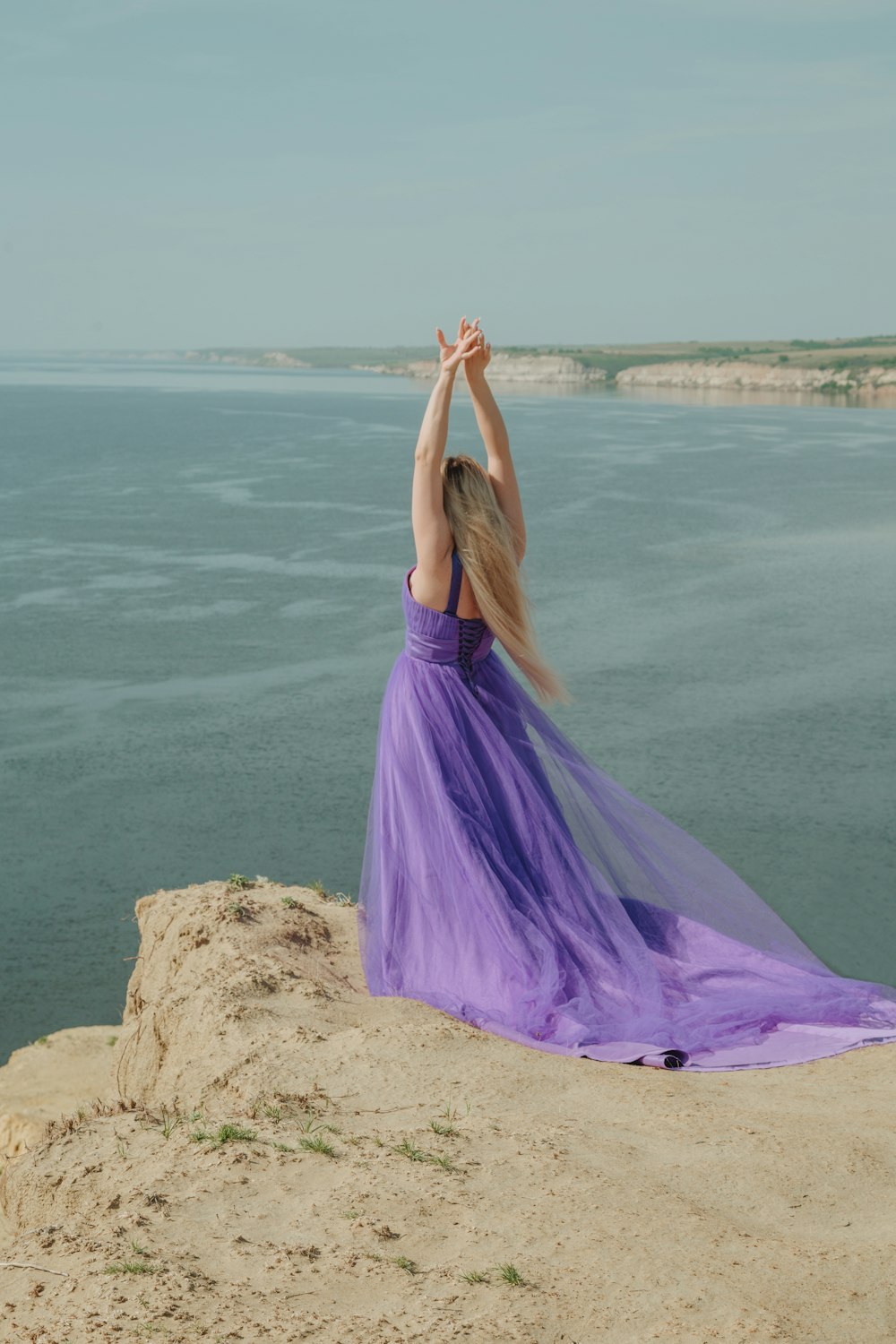 woman in purple dress standing on brown rock near body of water during daytime