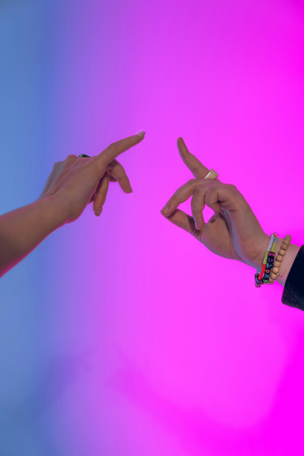 two hands reaching towards each other in front of a pink and blue background