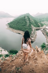 woman in white shirt sitting on rock formation near lake during daytime