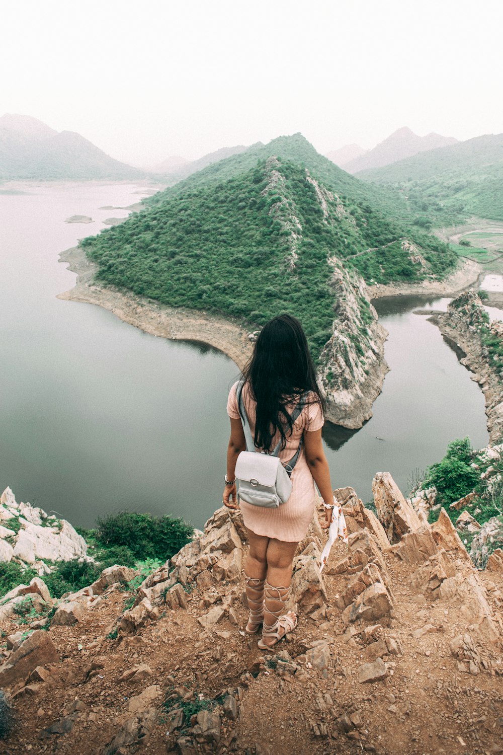 woman in white shirt sitting on rock formation near lake during daytime