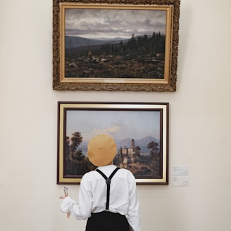 man in white dress shirt and black vest standing near painting of trees