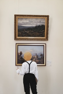 man in white dress shirt and black vest standing near painting of trees