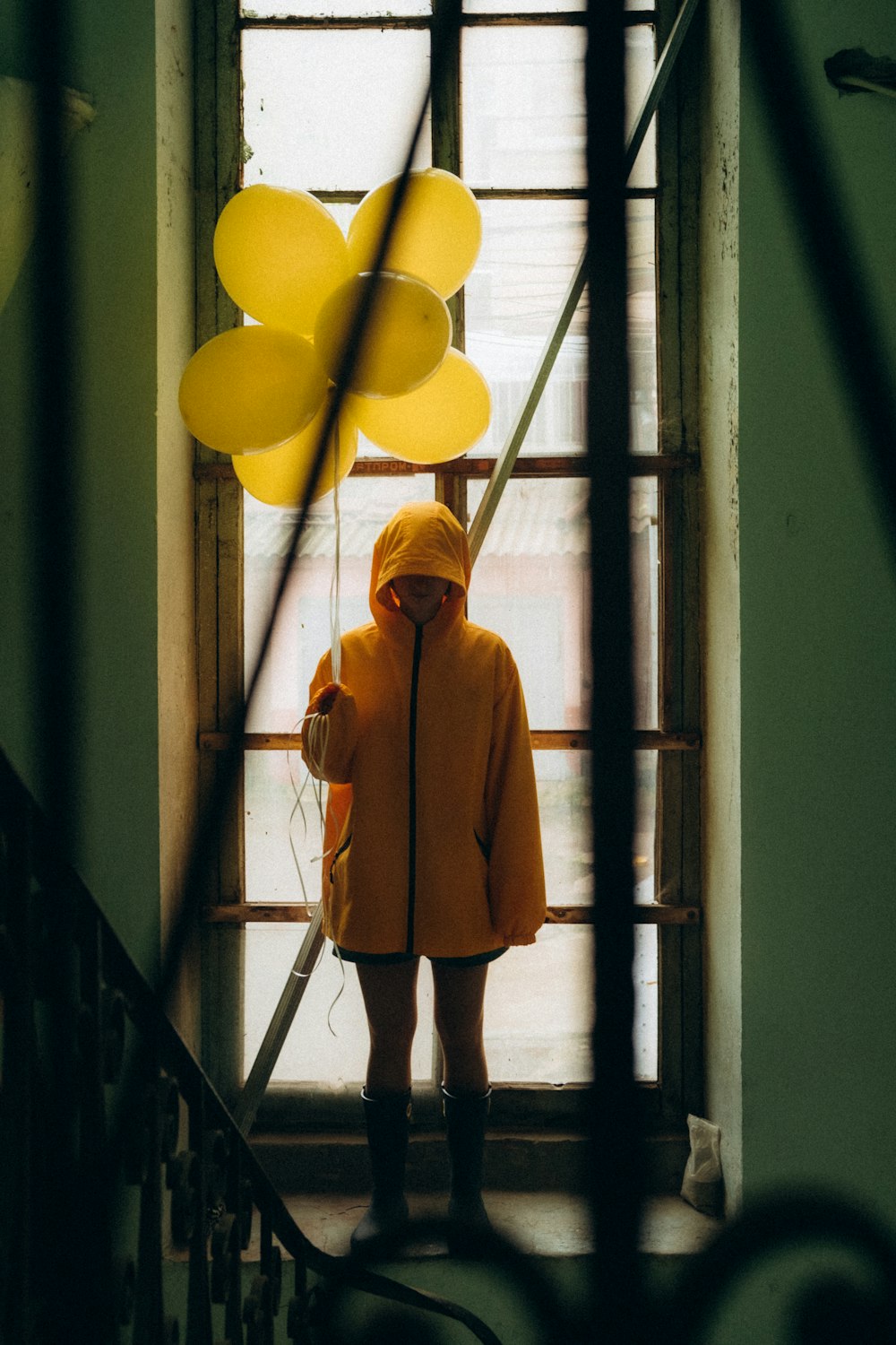 woman in brown coat standing beside yellow balloons