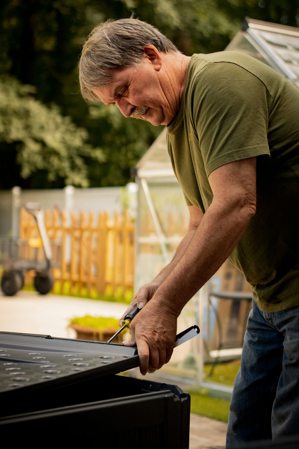 man in green crew neck t-shirt and blue denim jeans holding black and silver knife