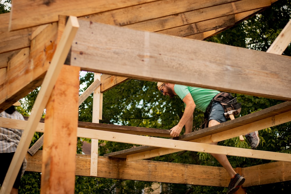 man in blue t-shirt and black shorts climbing on brown wooden bridge
