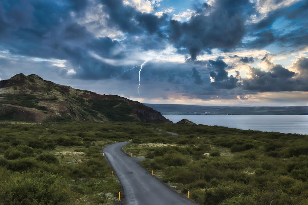 route en béton gris près d’un champ d’herbe verte sous un ciel nuageux bleu et blanc pendant la journée