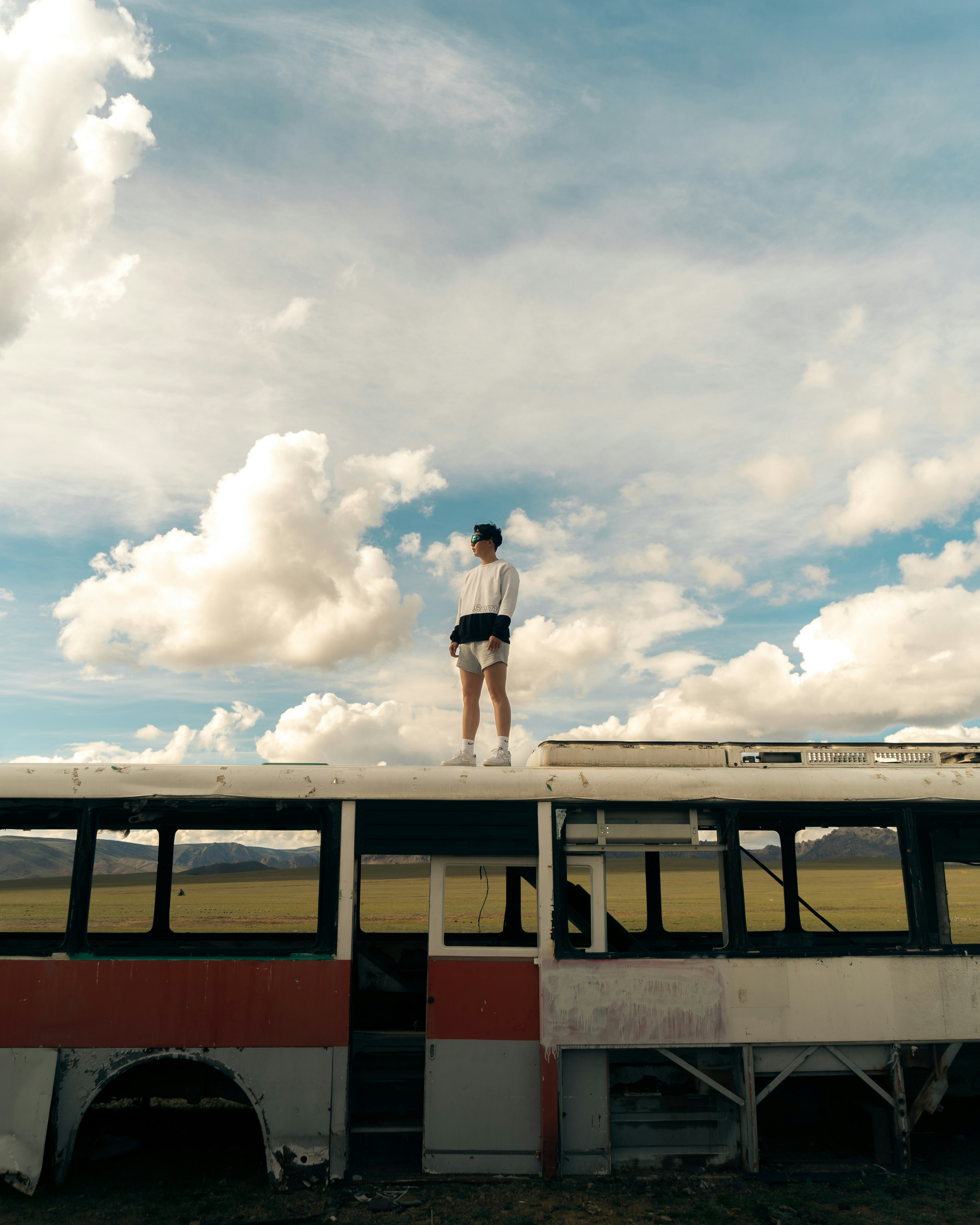 woman in white shirt and black shorts standing on red and white bus under white clouds