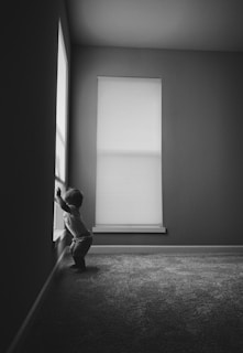 grayscale photo of man in long sleeve shirt and pants standing near window