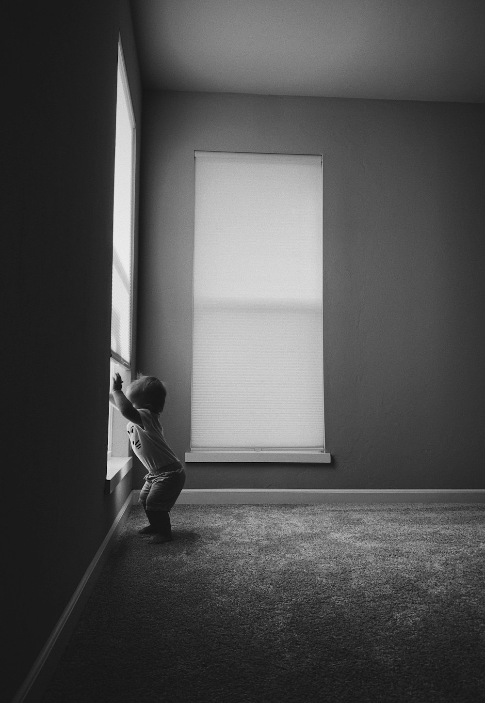 grayscale photo of man in long sleeve shirt and pants standing near window