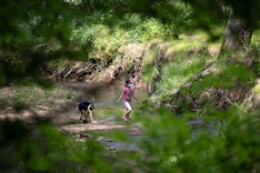 Children playing by a gentle stream with rolling green hills in the background.