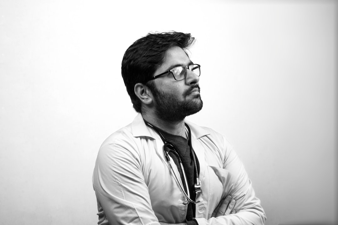 man in white dress shirt wearing black framed eyeglasses, Mid shot of a doctor looking above and thinking - Black and White