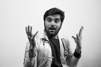 A person wearing a white coat and a stethoscope around their neck appears surprised or expressive with wide eyes and hands raised. The image is in black and white, emphasizing the contrast and expressions.