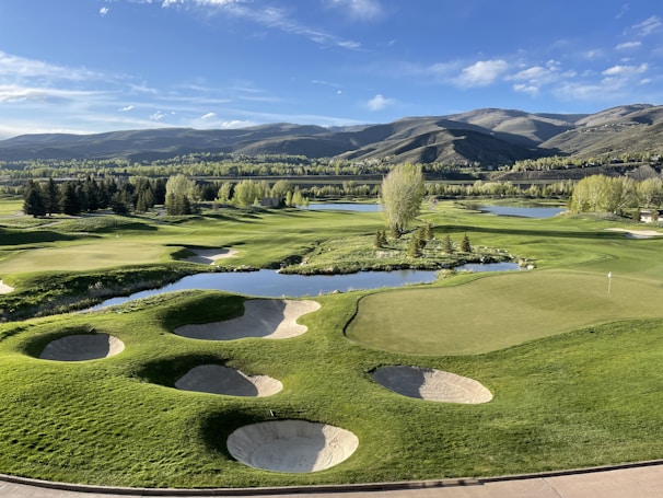 A panoramic view of a lush golf course with rolling fairways beside a calm river under a clear sky.