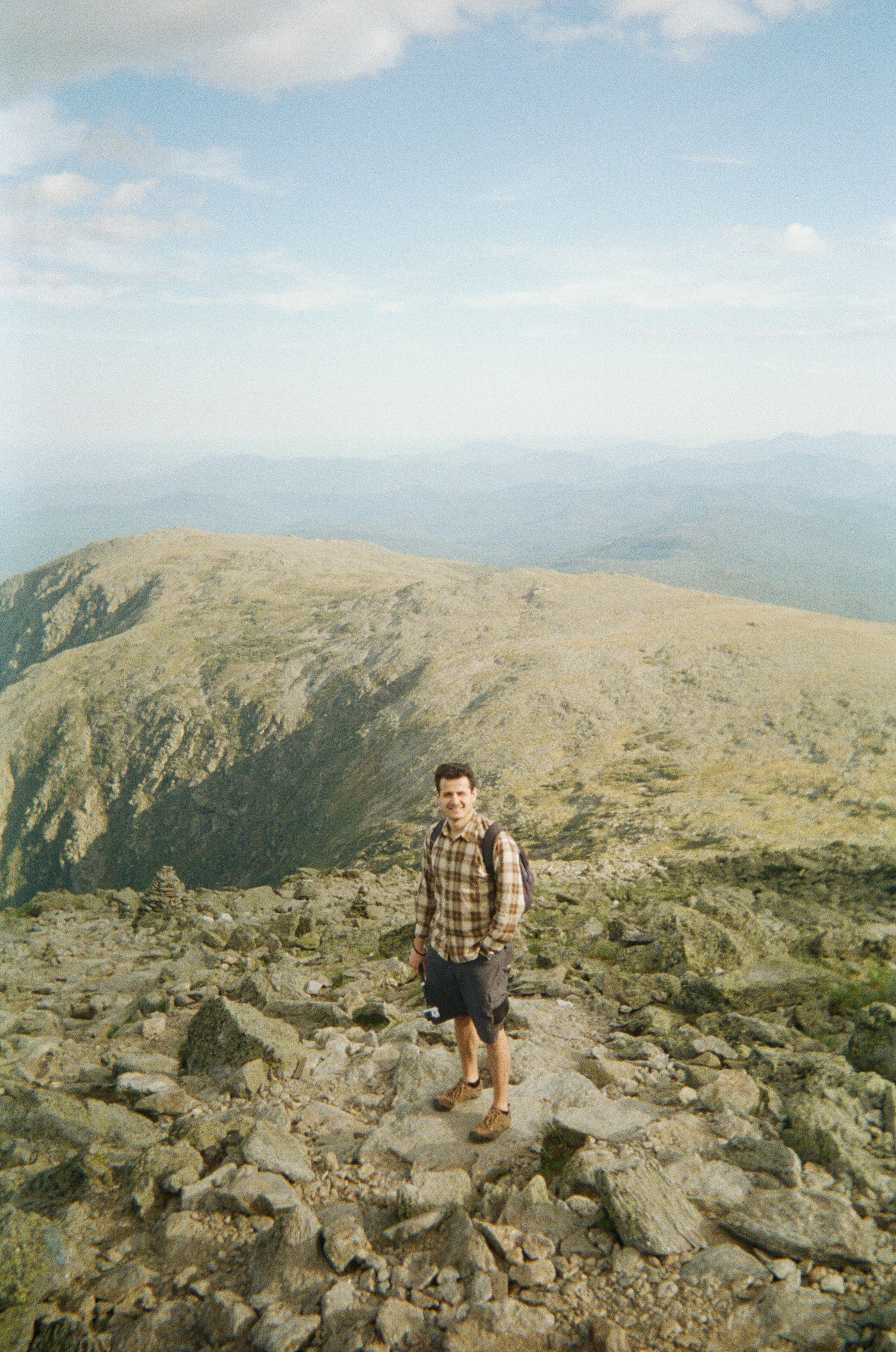 man in brown and black plaid shirt standing on rocky mountain during daytime