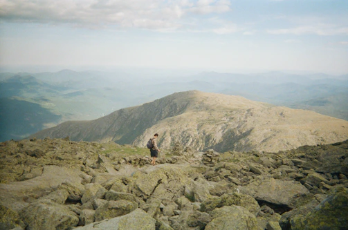 A panoramic mountain view with a lone male traveler hiking a rugged trail.