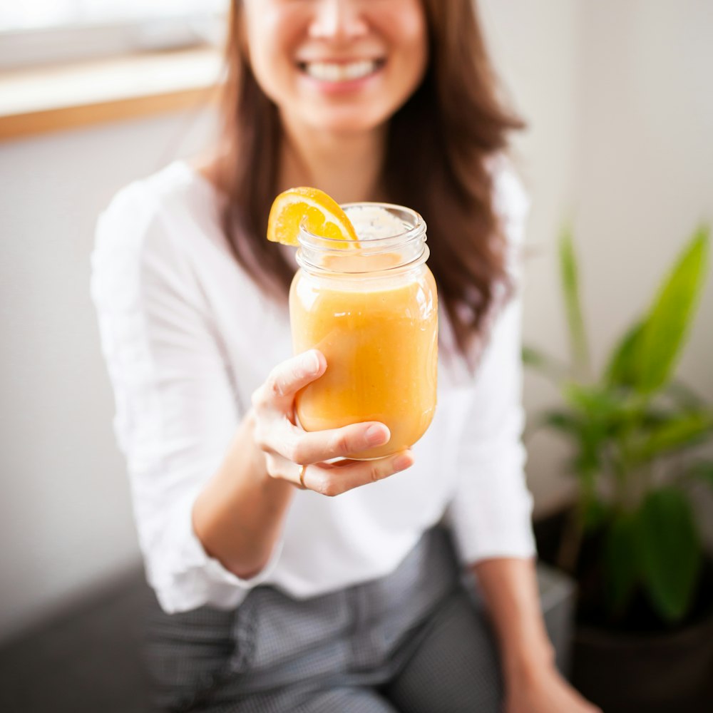 mulher sorridente segurando frasco de vidro transparente com líquido amarelo