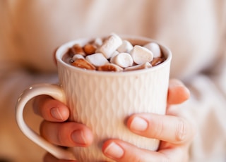 person holding white ceramic mug with brown and white beans