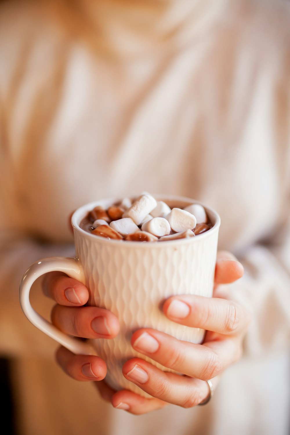 Person mit weißem Keramikbecher mit braunen und weißen Bohnen