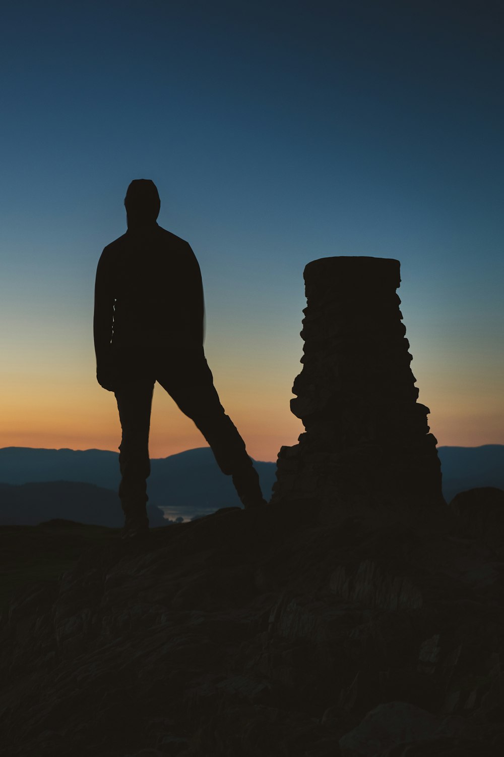 a man standing on top of a mountain next to a stack of rocks