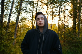 man in black hoodie standing in forest during daytime