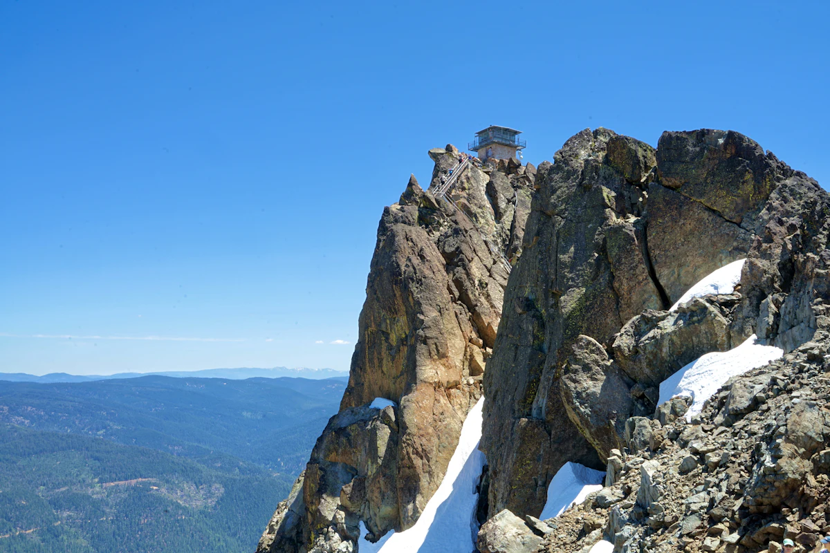 The fire lookout perched on a rock pinnacle on the Sierra Buttes, with snow below and forested ridges beyond
