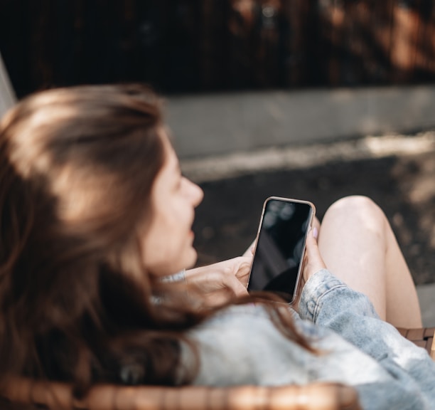 woman in white tank top lying on bed using black smartphone