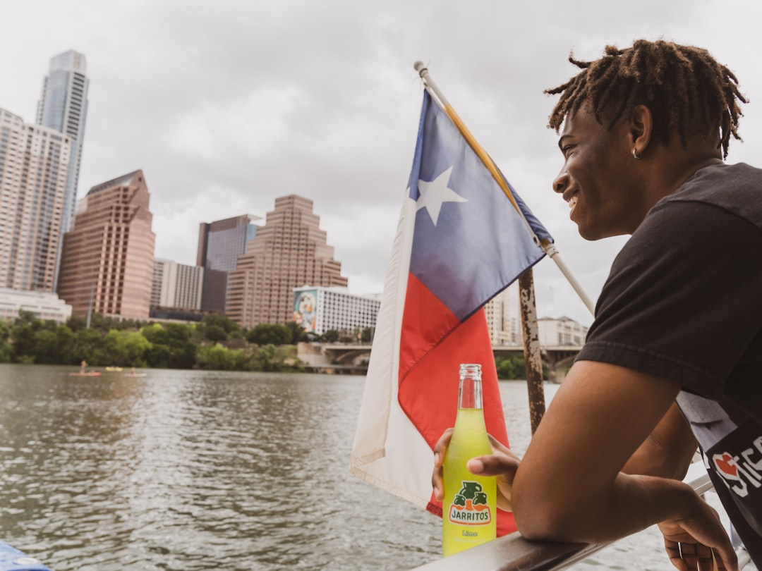 woman in black shirt holding yellow labeled bottle near body of water during daytime