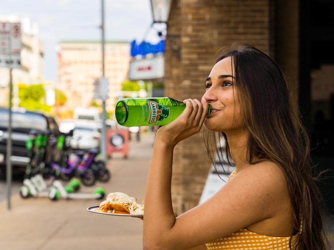 woman in white tank top drinking on green bottle