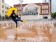 person in blue denim jeans and yellow umbrella walking on street during daytime